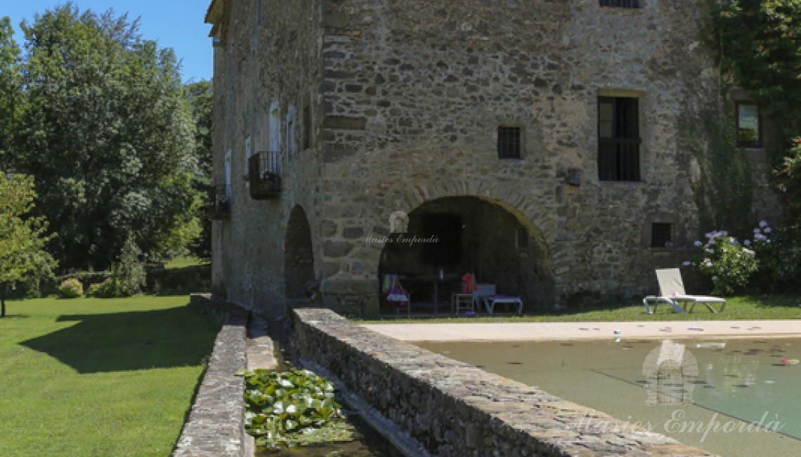 Vista de la piscina y la masía al fondo de la imagen 