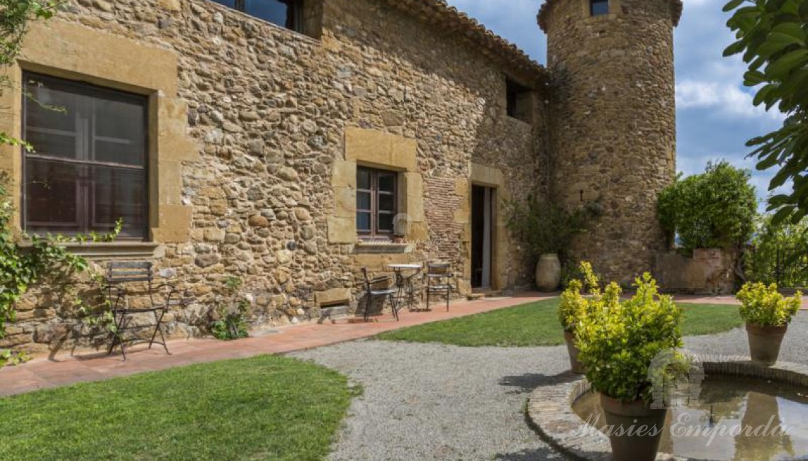 Vista del interior del patio superior de la casa con entrada lateral a la masía con torre circular de defensa y jardín con pequeño estanque. 