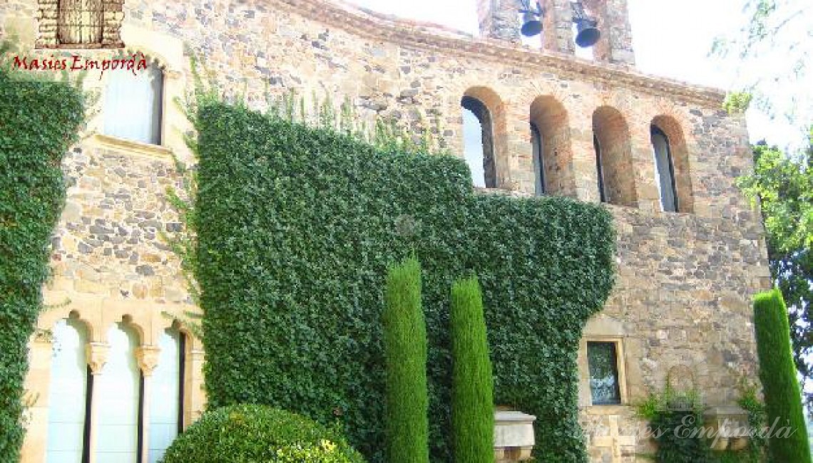 Detalle de los muros con la yedra recortada y fachadas de piedras del castillo con parte del jardín a la vista y el campanario de la iglesia que sobresale de la cubierta de tejas 