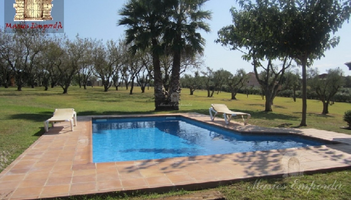 Vista de la piscina y solárium con el jardín al fondo de la imagen 