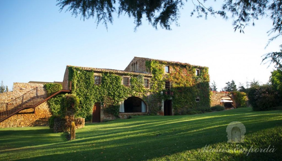 Vista de la masia al Baix Empordà i el jardí per la part interior d'aquest on s'aprecia la planta enfiladissa cobrint l'estructura de la casa en la seva totalitat.