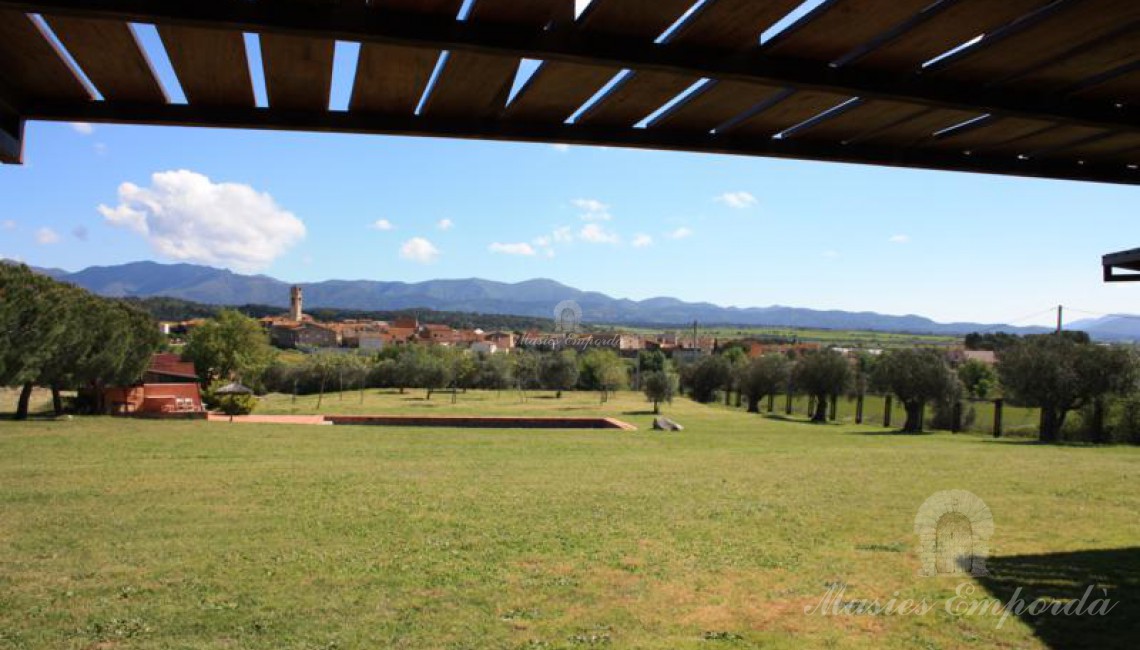 Vista de la piscina con porche y zona d barbacoa a la izquierda de la imagen con las montañas del macizo de La Albera al fondo