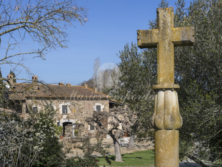 Detalle de la fachada de la masía con una cruz de piedra en primer plano