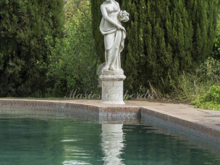 Vista de la piscina rodeada de cipreses con una preciosa estatua estilo romano