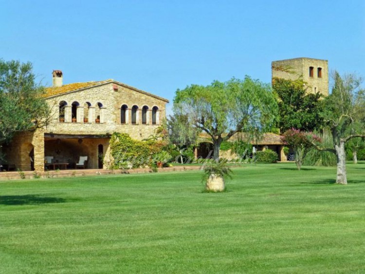 Vista lateral de la masía, los porches anexos y de la torre a ella con el jardín en primer plano.